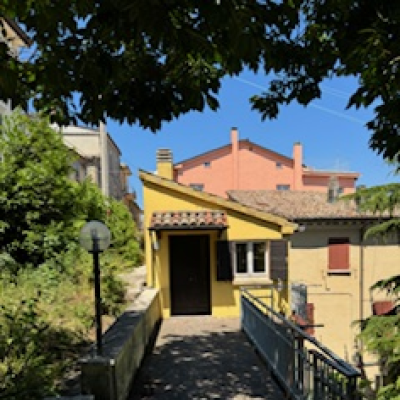 Casa gialla con terrazza, ombreggiata da alberi.