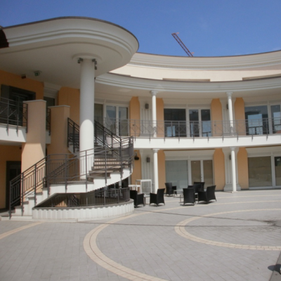 Edificio moderno con colonne e balconi, freccia gialla evidenzia ingresso.